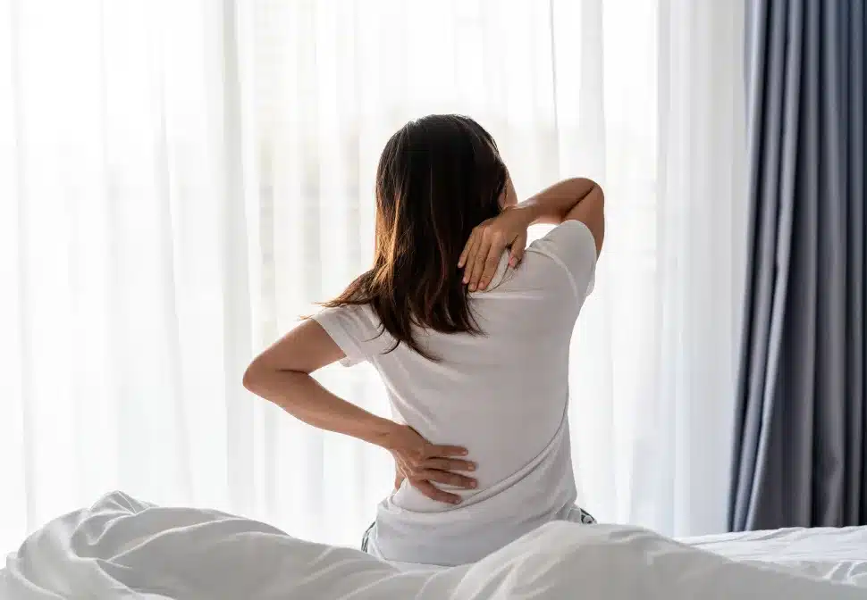 Paciente sentindo dor lombar ao levantar da cama, ilustrando as causas da rigidez matinal e tratamentos especializados com a Dra. Natally Santiago em São Paulo.